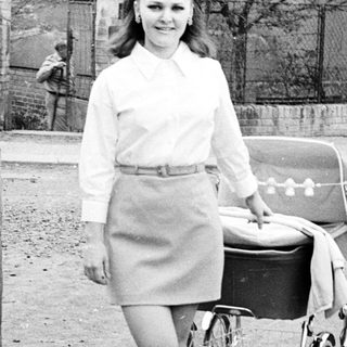 Woman with vintage pram walking on a paved road.