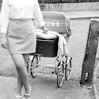 Woman with vintage pram walking on a paved road.