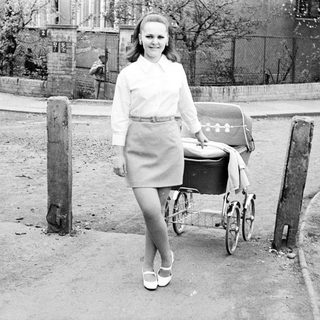 Woman with vintage pram walking on a paved road.