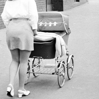 Woman walks away, pushing a vintage baby carriage.