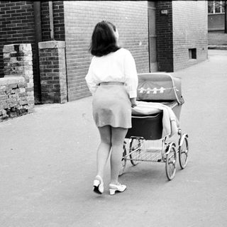 Woman walks away, pushing a vintage baby carriage.