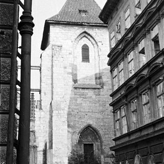 Stone tower with arched gateway, surrounded by buildings.