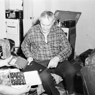 Couple seated, presenting a box of chocolates in a home.