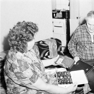 Couple seated, presenting a box of chocolates in a home.