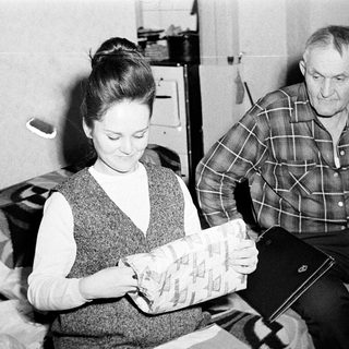 Woman examines package; man watches nearby.