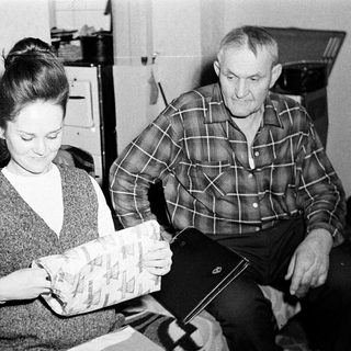 Woman examines package; man watches nearby.