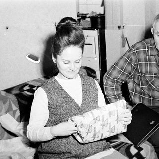 Woman examines package; man watches nearby.