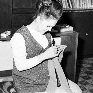 Woman seated, sewing fabric in a mid-century home.