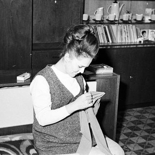 Woman seated, sewing fabric in a mid-century home.