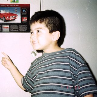 Boy points at "First Mustang" poster on a door.