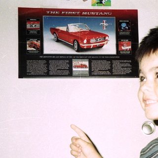 Boy points at "First Mustang" poster on a door.