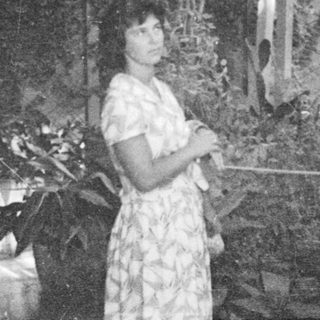 Woman stands near statue, surrounded by tropical foliage.