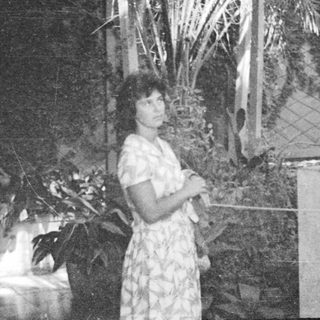 Woman stands near statue, surrounded by tropical foliage.