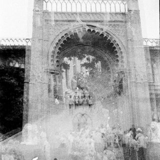 Monumental archway with figures gathered below, captured in grayscale.