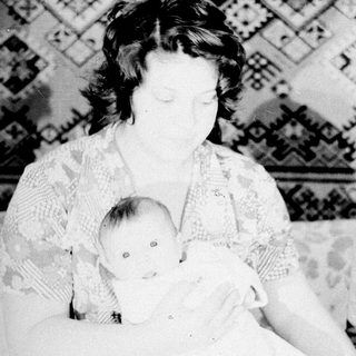 Woman holding baby, child standing nearby in a room.