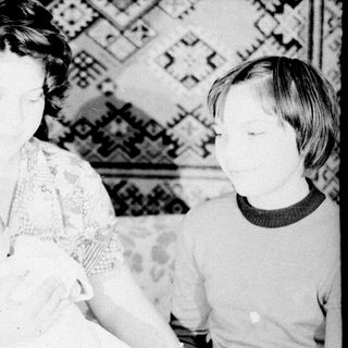 Woman holding baby, child standing nearby in a room.