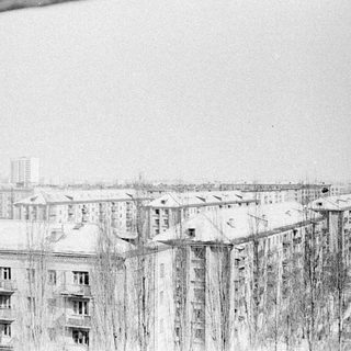 Snowy cityscape with apartment buildings and bare trees.