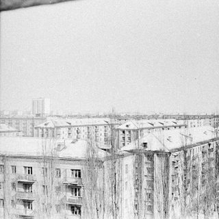 Snowy cityscape with apartment buildings and bare trees.