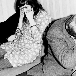 Here's a brief summary of the image: Man comforting a woman, seated on a sofa.