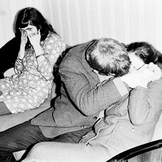 Here's a brief summary of the image: Man comforting a woman, seated on a sofa.