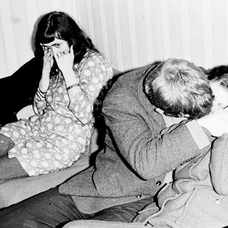 Here's a brief summary of the image: Man comforting a woman, seated on a sofa.