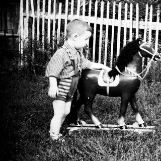 Two young boys stand near a wooden rocking horse.