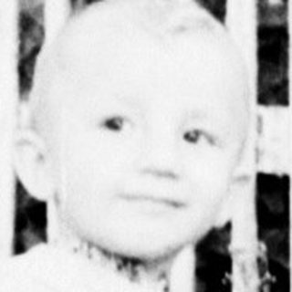 Child rides a wooden horse in a grassy yard.