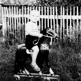 Child rides a wooden horse in a grassy yard.