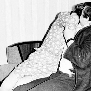 Here's a brief summary of the image: Couple embraces and kisses on a sofa.