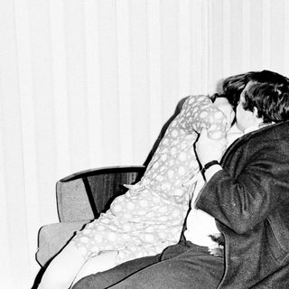 Here's a brief summary of the image: Couple embraces and kisses on a sofa.