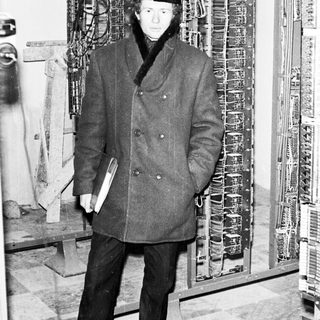 Man in coat stands near a complex electrical panel.