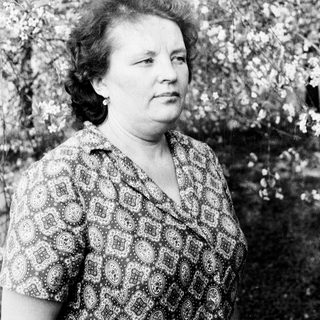 Black and white portrait of a woman standing near blooming trees.