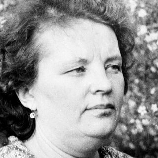 Black and white portrait of a woman standing near blooming trees.