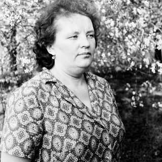 Black and white portrait of a woman standing near blooming trees.