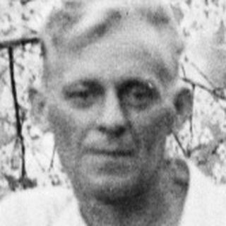 Man stands near a blossoming tree in a garden.