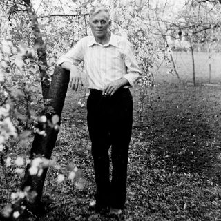 Man stands near a blossoming tree in a garden.