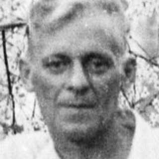 Man stands near a tree in a garden setting.