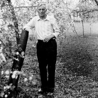 Man stands near a tree in a garden setting.