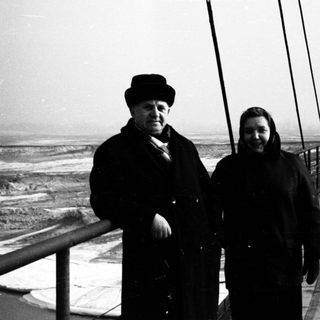 Couple stands on a rope bridge overlooking a wintry landscape.