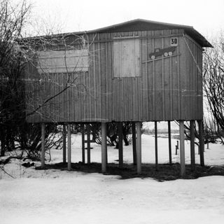 Elevated, weathered shed sits in a snowy, winter landscape.