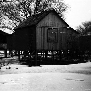 Elevated, weathered buildings stand in a snowy, wintry landscape.