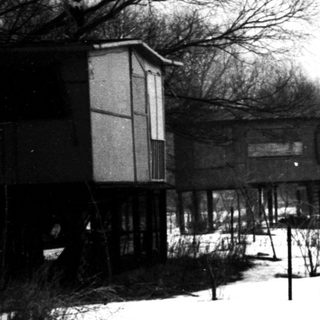 Winter village scene with elevated houses and snow-covered ground.