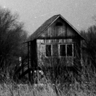Winter scene with a weathered house and overgrown field.