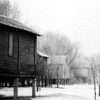 Snow-covered village with wooden houses and bare trees.