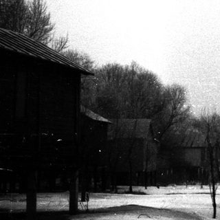 Snow-covered village with bare trees and wooden buildings.