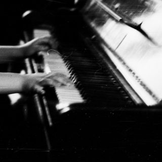 Young girl plays piano, seated in a vintage room.