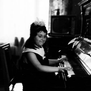Young girl plays piano, seated in a vintage room.