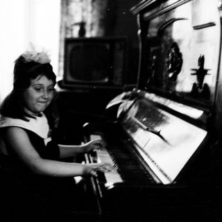 Young girl plays piano, seated in a vintage room.