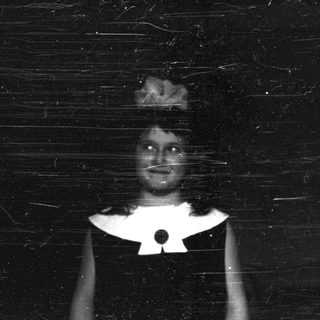 Here's a brief summary of the image: Faded black and white portrait of a person in a dress.