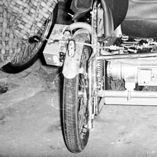 Man seated next to a vintage, three-wheeled vehicle.